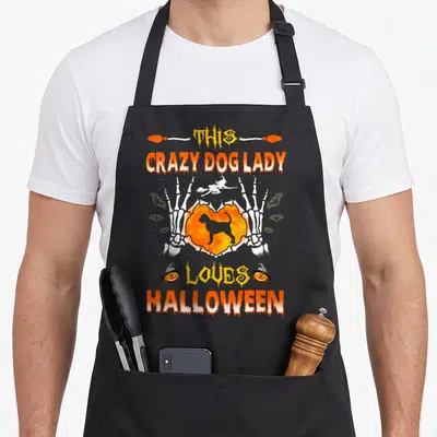 Bloodhound halloween dog apron - Dog silhouette in orange heart held by skeleton hands with Halloween text — shown on a black cotton canvas apron against a white background