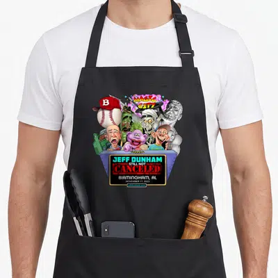 Dunham birmingham apron - Jeff Dunham puppets on blue stage with Magic City text and baseball — shown on a black cotton canvas apron against a white background