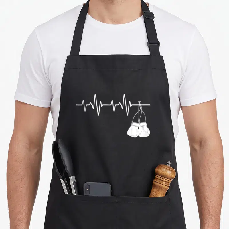 Heartbeat kickboxing apron - White heartbeat line with a pair of boxing gloves hanging from the right end — shown on a black cotton canvas apron against a white background