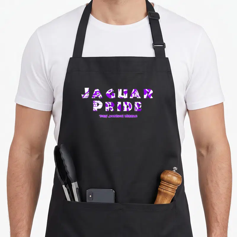 Cute pride apron - JAGUAR PRIDE text filled with purple and white animal spots above Toby Johnson Middle — shown on a black cotton canvas apron against a white background