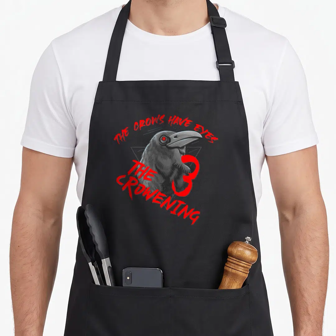 Eye funny crow apron - Cartoon crow holding red 3 with THE CROWS HAVE EYES and THE CROWENING text — shown on a black cotton canvas apron against a white background