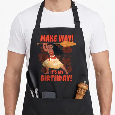 Way princess apron - Woman holding paddle with Make Way Its My Birthday text and brown leaves — shown on a black cotton canvas apron against a white background