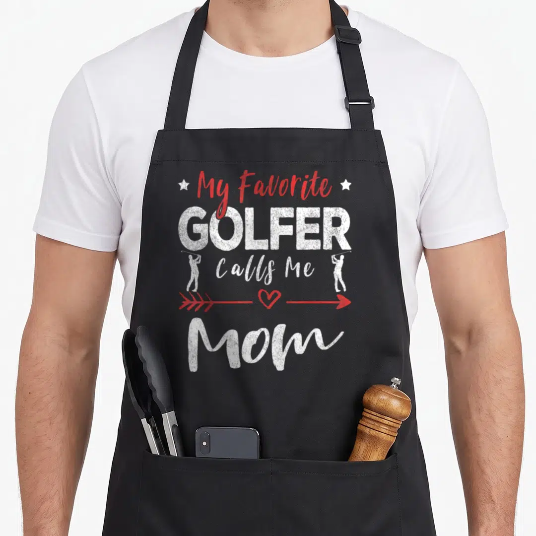 Golfer call golf apron - My Favorite Golfer Calls Me Mom text with two golfer silhouettes and red heart arrow — shown on a black cotton canvas apron against a white background