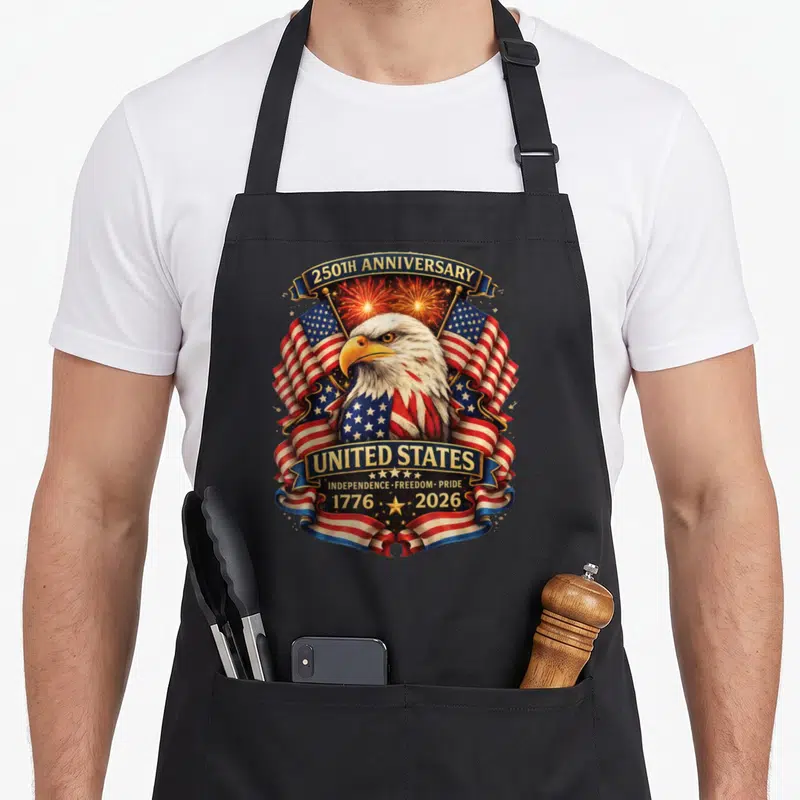 Independence eagles grill apron - Bald eagle with USA flags fireworks and 250th anniversary text banners — shown on a black cotton canvas apron against a white background