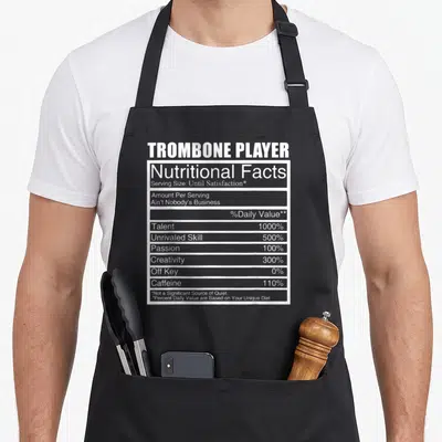 Trombone arcadia apron - White typographic nutritional facts label reading Trombone Player with 1000% talent and 0% off — shown on a black cotton canvas apron against a white background