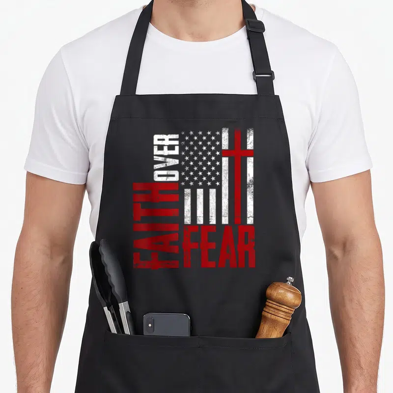 Christianity cross over apron - Distressed US flag with red cross and vertical FAITH OVER FEAR text — shown on a black cotton canvas apron against a white background