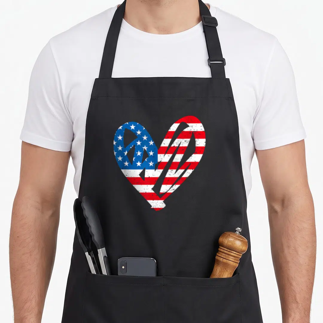 Partiotic 4th of july apron - Distressed heart shape filled with red white and blue USA flag pattern — shown on a black cotton canvas apron against a white background