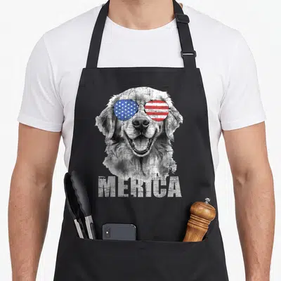 Merica golden retriever apron - Distressed dog head wearing American flag sunglasses above MERICA text — shown on a black cotton canvas apron against a white background