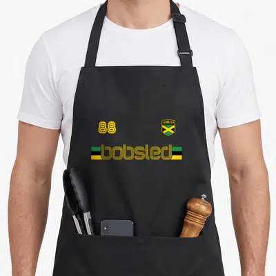 Jamaican flag bobsled apron - Yellow 88 and Jamaica shield above bobsled text flanked by green black and yellow bars — shown on a black cotton canvas apron against a white background