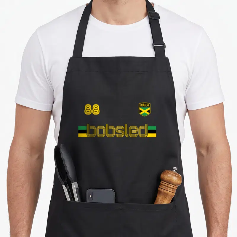 Jamaican flag bobsled apron - Yellow 88 and Jamaica shield above bobsled text flanked by green black and yellow bars — shown on a black cotton canvas apron against a white background