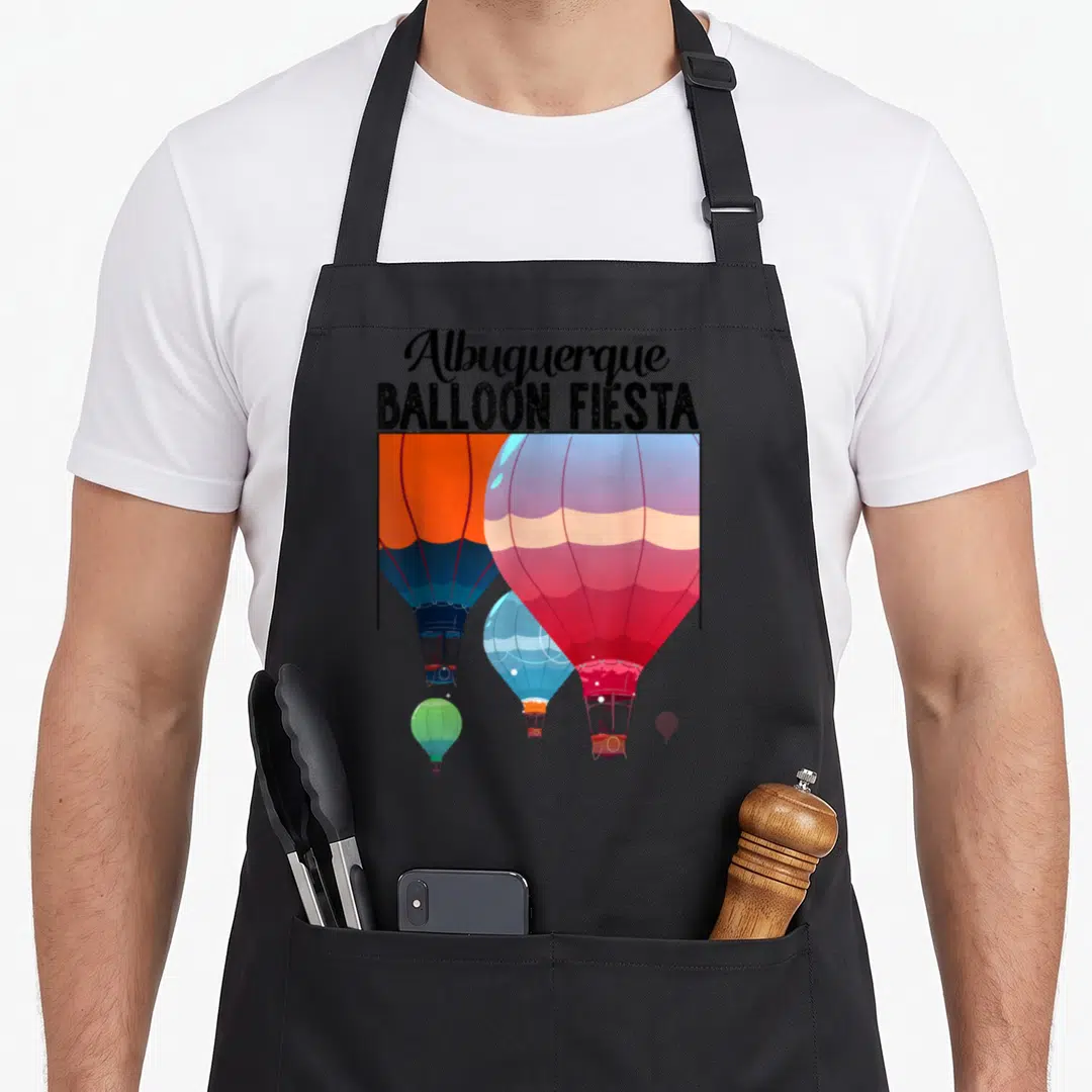Balloon fiesta mexico apron - Stacked text above red, blue, orange, pink, green, and black hot air balloons in cartoon — shown on a black cotton canvas apron against a white background