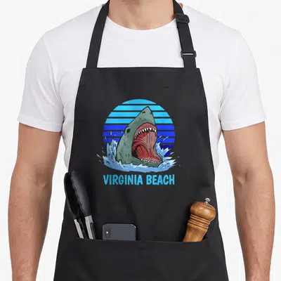 Virginia theme aprons - Cartoon shark head with red mouth and blue striped sun above text — shown on a black cotton canvas apron against a white background