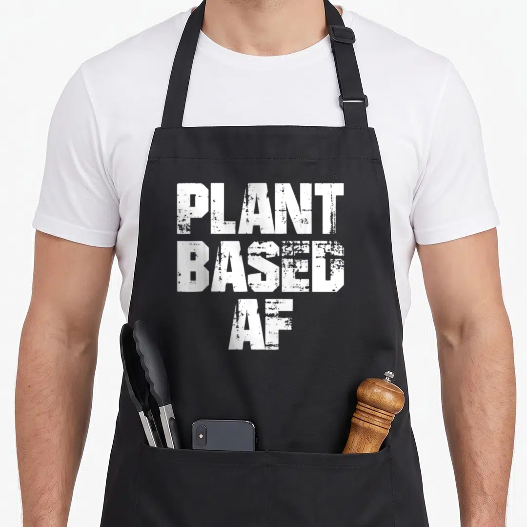Fitness plant based apron - White distressed text PLANT BASED AF stacked vertically on black fabric — shown on a black cotton canvas apron against a white background