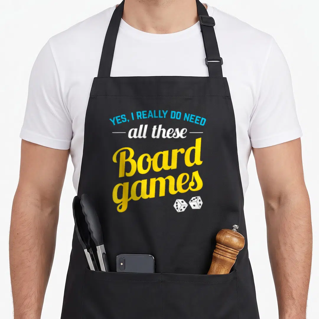 Gamer do i need an apron - Stacked text YES I REALLY DO NEED all these Board games with two dice in blue white yellow — shown on a black cotton canvas apron against a white background