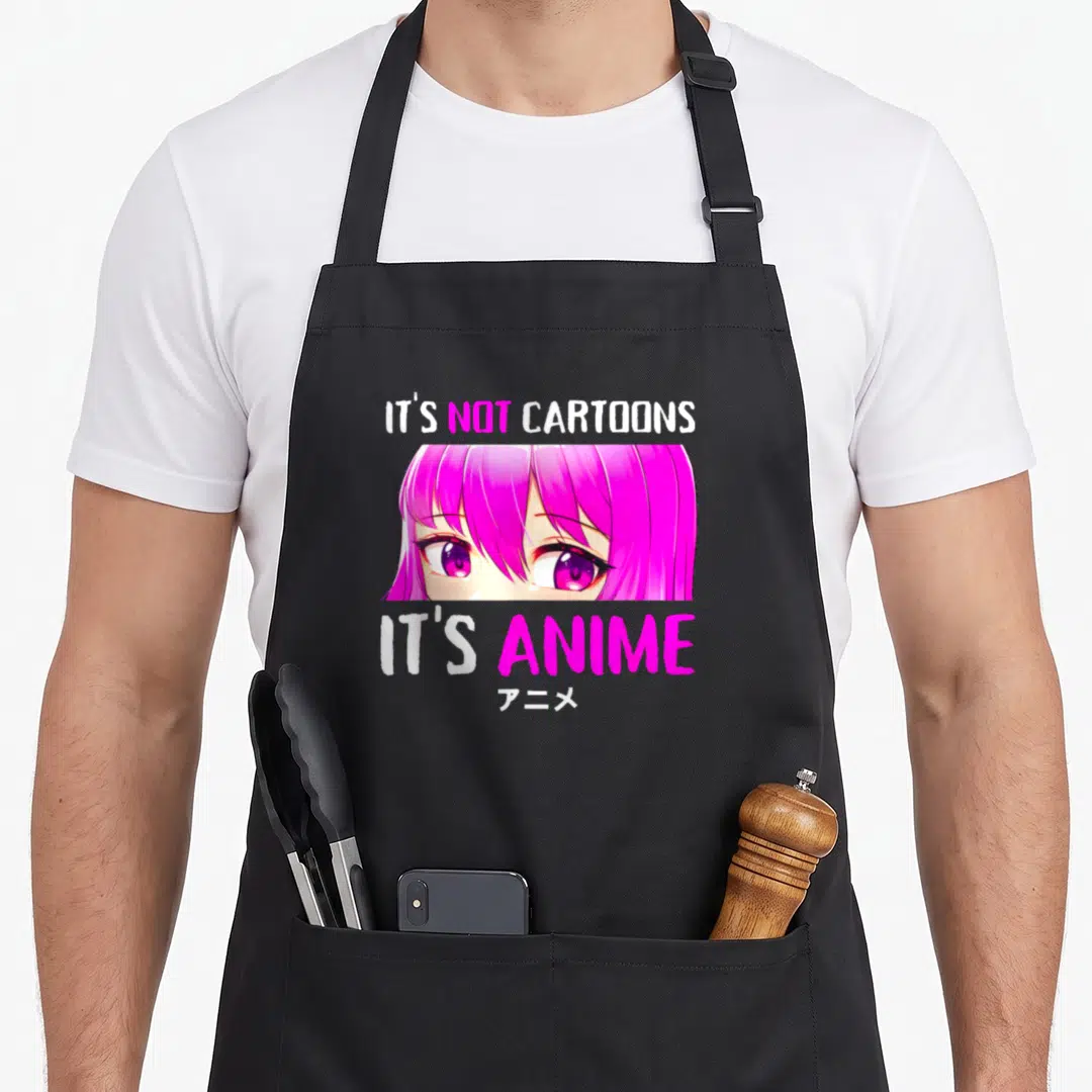 Manga cartoon apron - Anime girl face with pink hair and purple eyes surrounded by IT'S NOT CARTOONS IT'S ANIME text — shown on a black cotton canvas apron against a white background