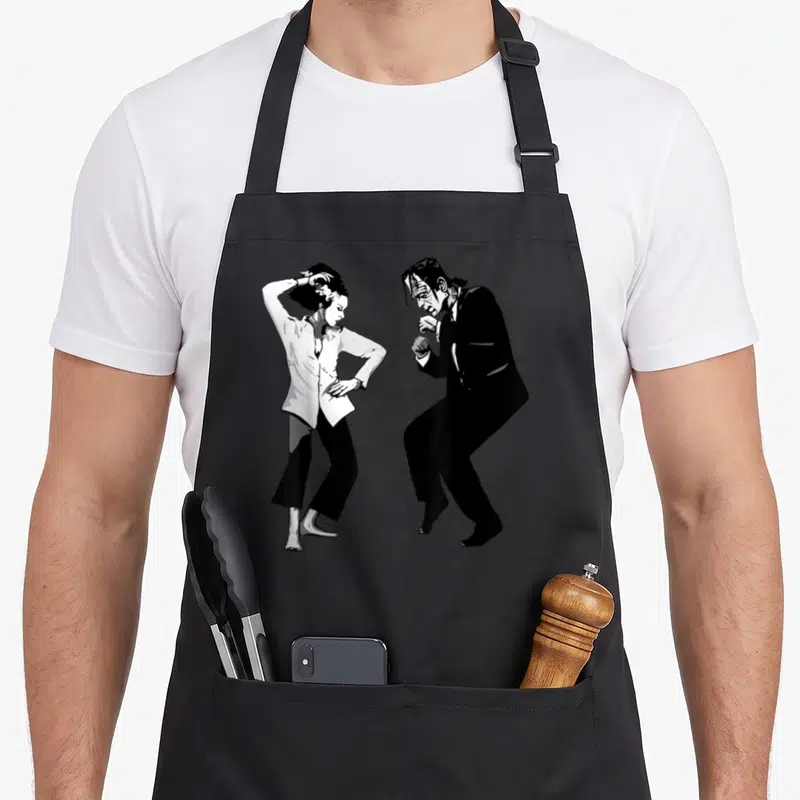 Bride halloween apron - Black and white line art of Frankenstein and Bride dancing side-by-side — shown on a black cotton canvas apron against a white background