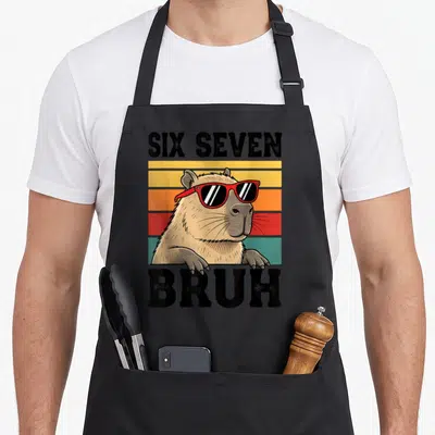 Seven bruh meme apron - Retro tan capybara with red sunglasses on yellow orange red and teal stripes with black text — shown on a black cotton canvas apron against a white background