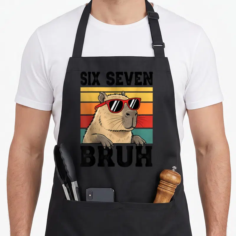 Seven bruh meme apron - Retro tan capybara with red sunglasses on yellow orange red and teal stripes with black text — shown on a black cotton canvas apron against a white background