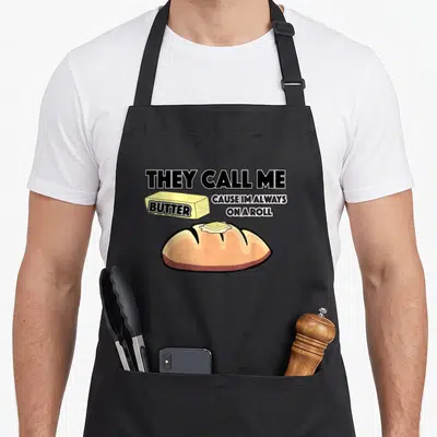 They bread apron - Stacked text they call me butter cause im always on a roll around yellow butter stick and brown — shown on a black cotton canvas apron against a white background