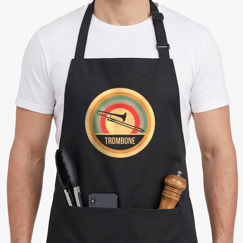 Trombonist trombone quotes apron - Grey trombone silhouette on tan orange green red and blue concentric circles — shown on a black cotton canvas apron against a white background