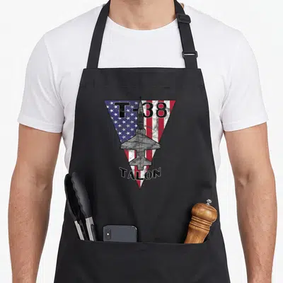 Talon patriotic apron - Distressed T-38 Talon jet over inverted US flag triangle with black text — shown on a black cotton canvas apron against a white background