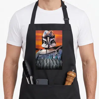 Captain t-rex apron - Helmeted soldier over flying spaceships and standing stormtroopers on orange background — shown on a black cotton canvas apron against a white background