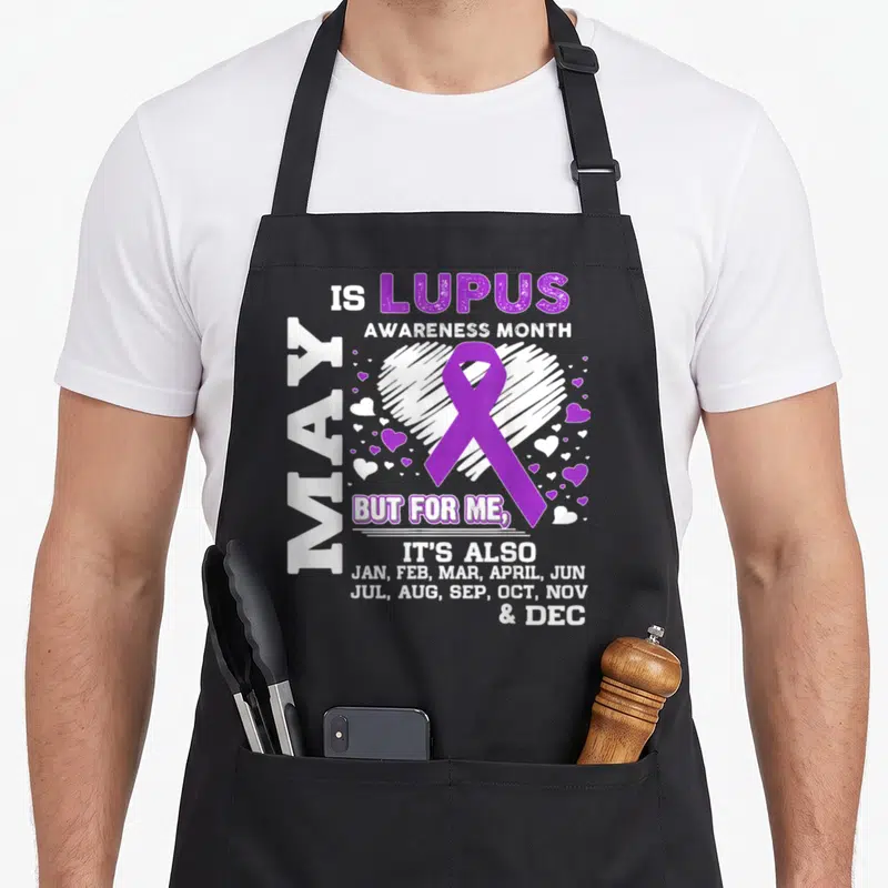 May lupus awareness apron - Purple ribbon over sketched white heart with text listing all twelve months of the year — shown on a black cotton canvas apron against a white background