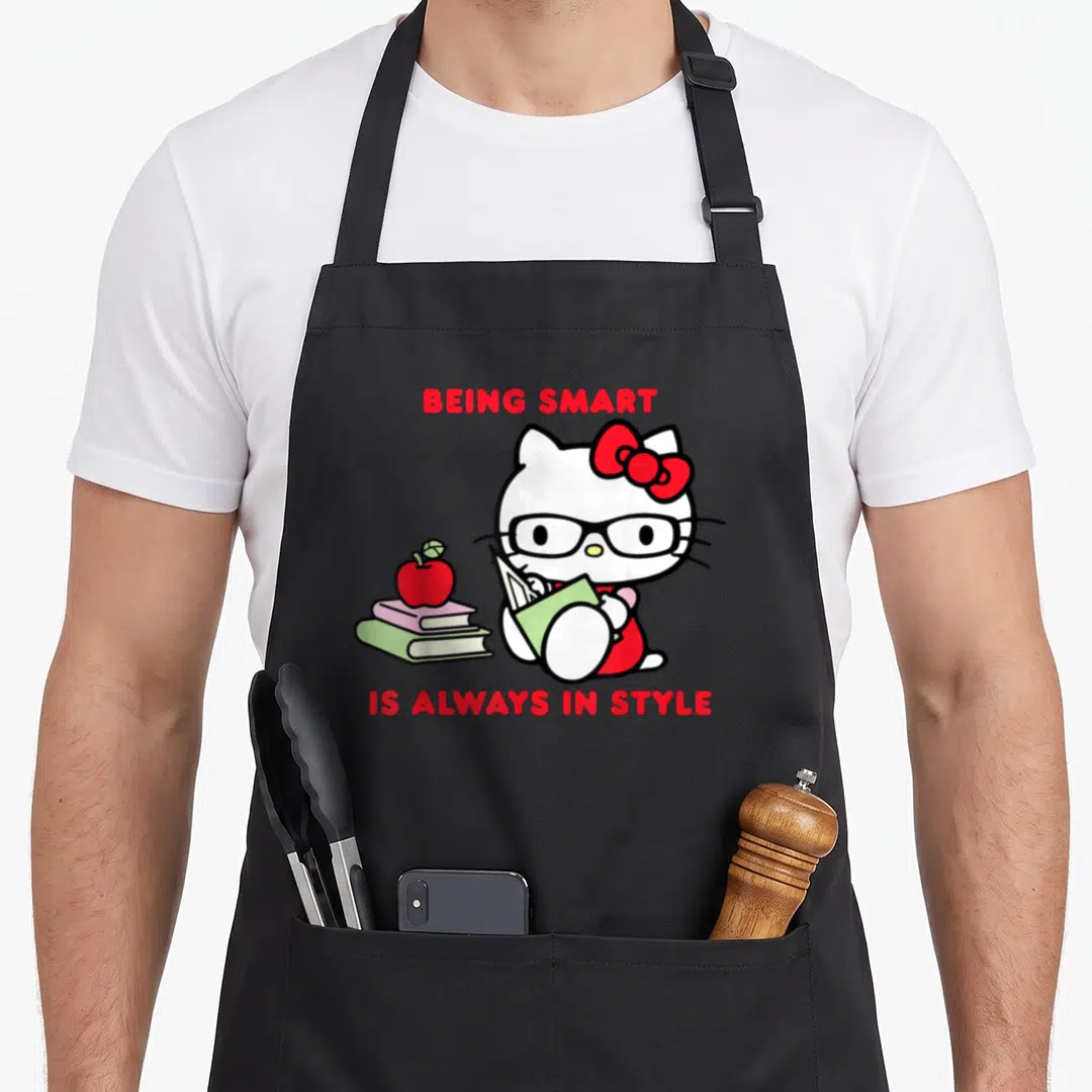 Alway smart apron - Hello Kitty glasses reading green book stack two books red apple — shown on a black cotton canvas apron against a white background