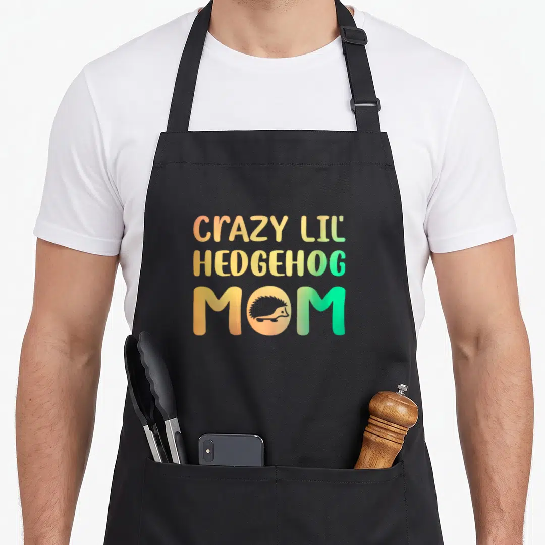 Lil crazy hedgehog lady apron - Stacked text CRAZY LIL HEDGEHOG MOM with hedgehog silhouette in O, orange yellow green — shown on a black cotton canvas apron against a white background