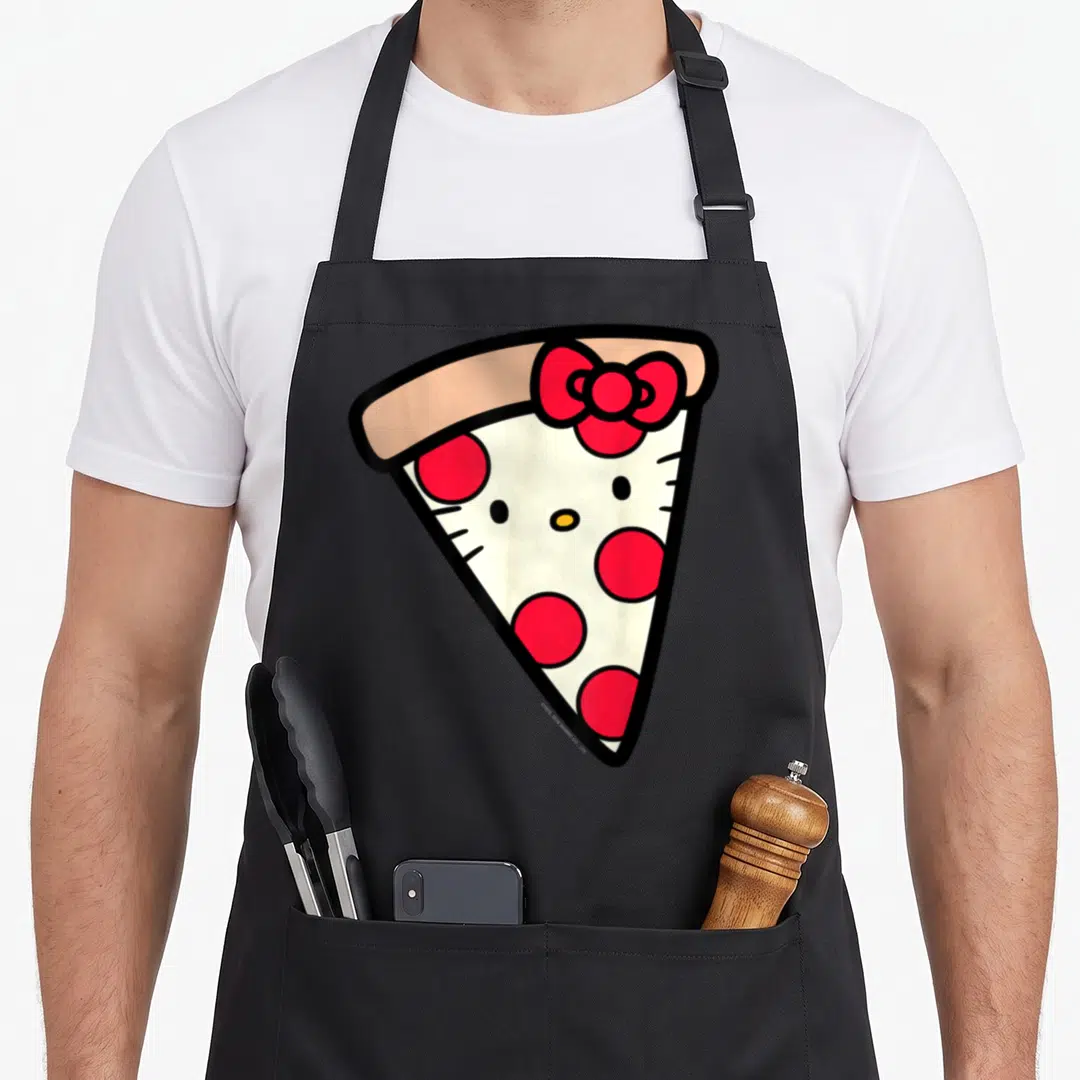 Slice pizza apron - Cartoon pizza slice with tan bow and red pepperoni cheeks forming a character face — shown on a black cotton canvas apron against a white background
