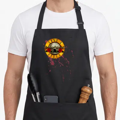 Splatter rose apron - Guns N' Roses logo with red splatters, yellow circle, and crossed revolvers — shown on a black cotton canvas apron against a white background