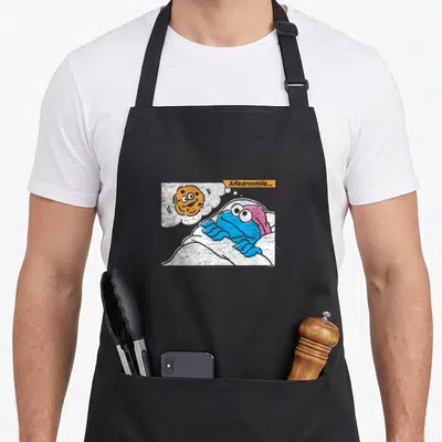 Meanwhile cookie monster apron - Blue monster lying in bed with cookie thought bubble and meanwhile text — shown on a black cotton canvas apron against a white background