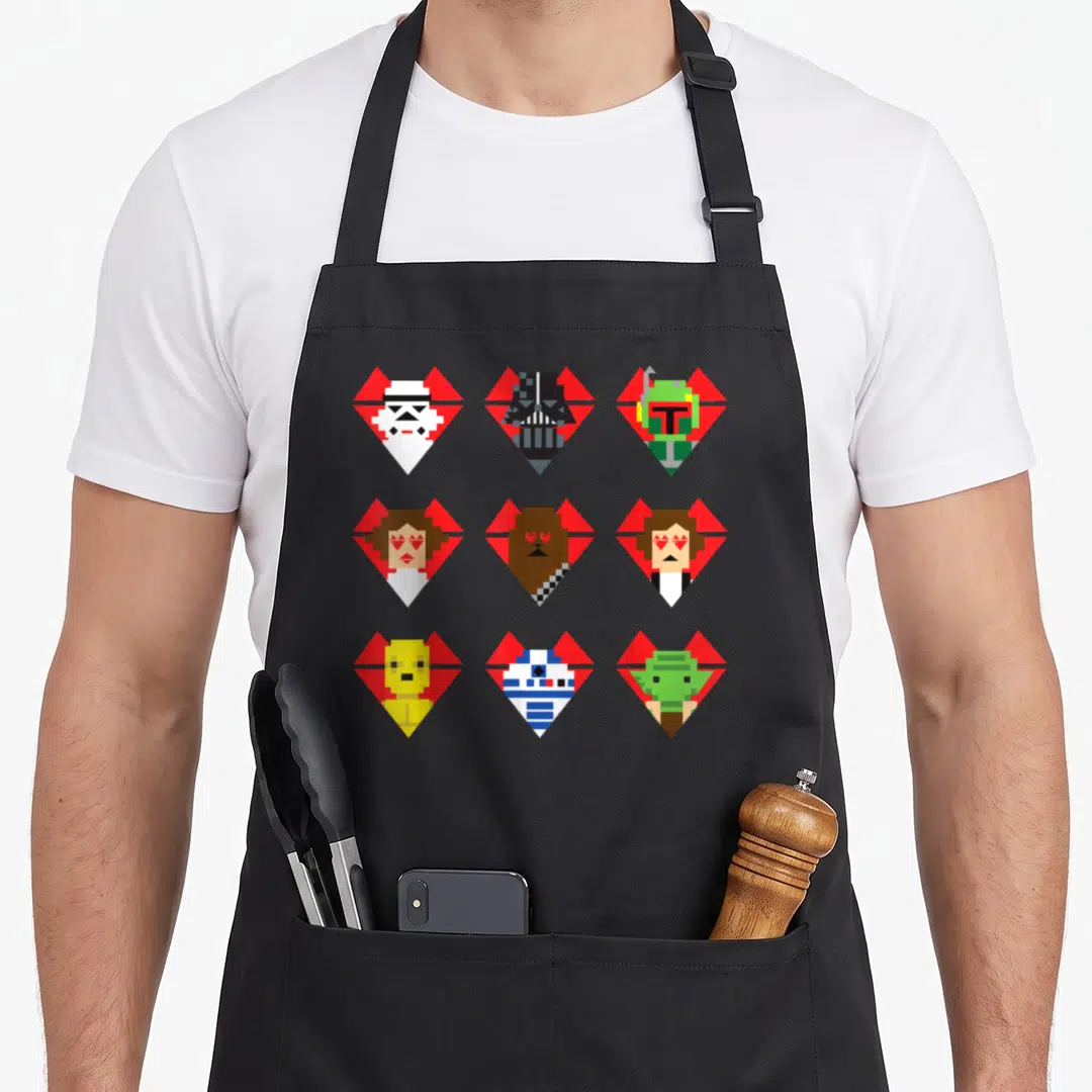 Pixel valentine apron - Nine pixel art heads in red hearts arranged in a 3x3 grid using retro colors — shown on a black cotton canvas apron against a white background