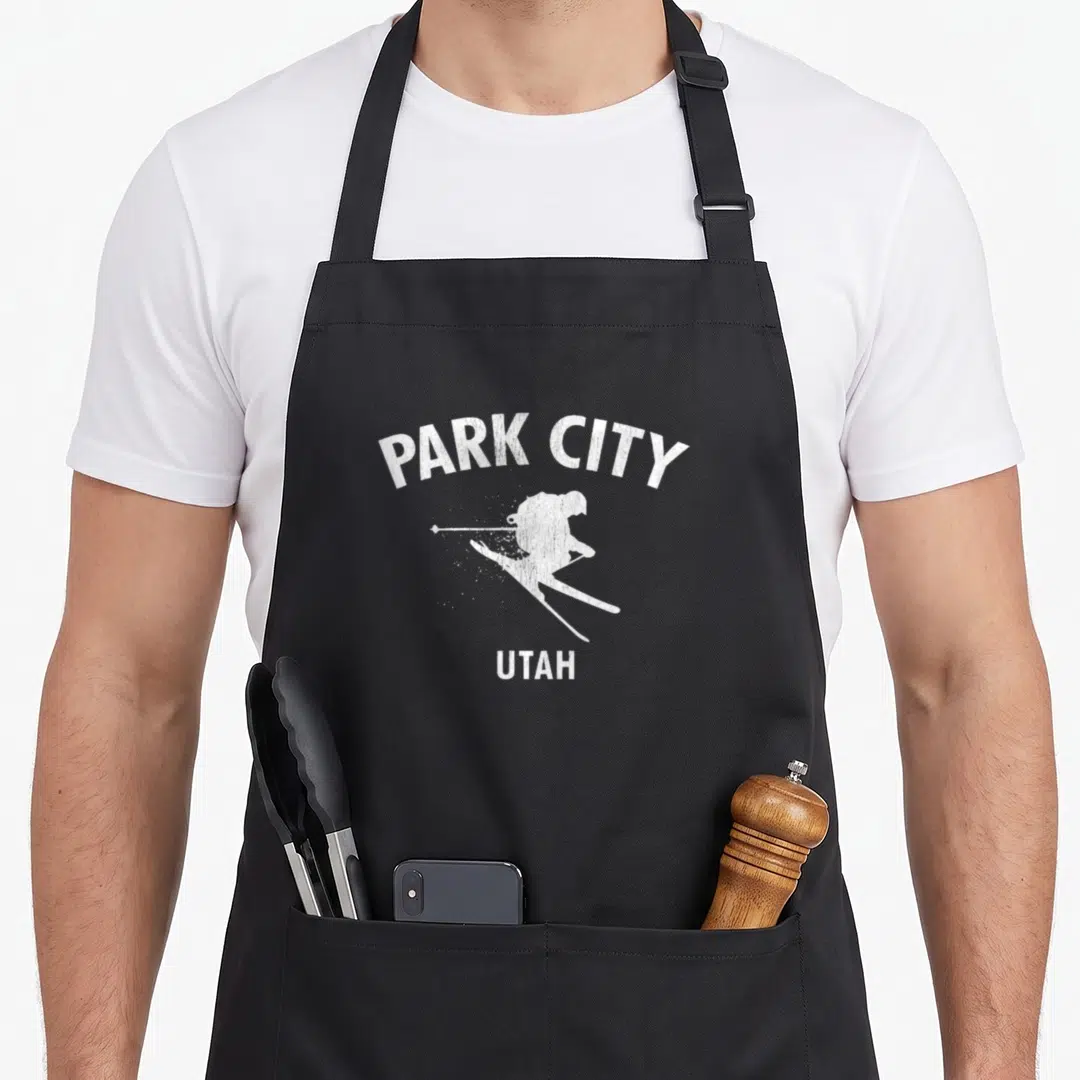 Park ski girl apron - White distressed skier silhouette with Park City Utah text — shown on a black cotton canvas apron against a white background