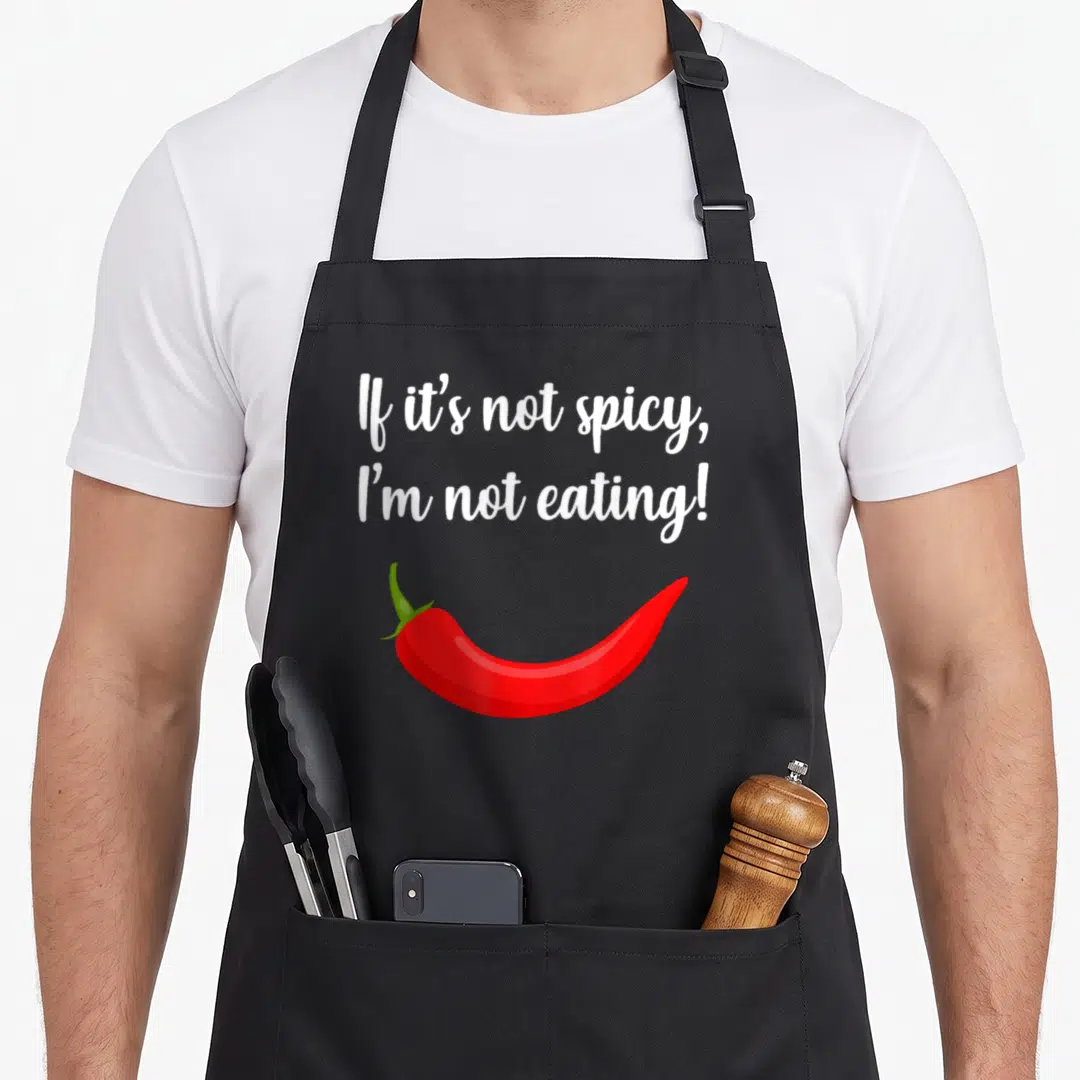 Adventure thai food apron - White script reading If it's not spicy I'm not eating above a red cartoon chili pepper — shown on a black cotton canvas apron against a white background