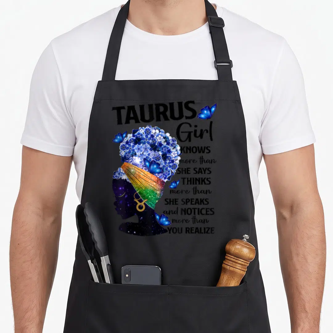 Sweet taurus aprons - Woman profile with blue flower hair and text about Taurus Girl knowing more than she says — shown on a black cotton canvas apron against a white background