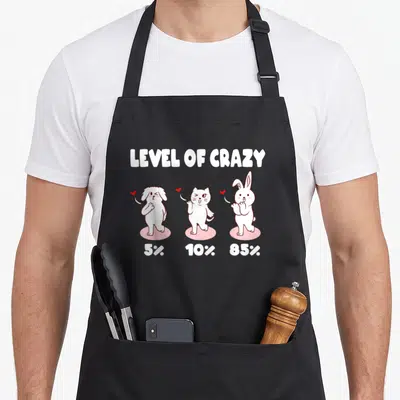 Percent cat apron - LEVEL OF CRAZY text above dog cat rabbit on pink circles with hearts — shown on a black cotton canvas apron against a white background