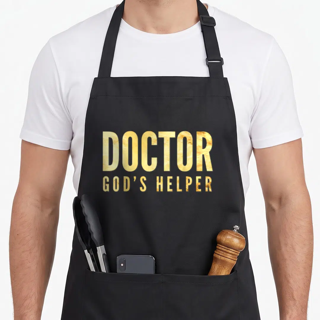 God doctor apron - Gold DOCTOR GOD'S HELPER typography on grey background — shown on a black cotton canvas apron against a white background
