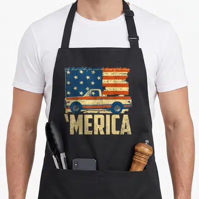 Merica american flag apron - Distressed US flag with vintage pickup truck overlay, script text above, 'MERICA below — shown on a black cotton canvas apron against a white background
