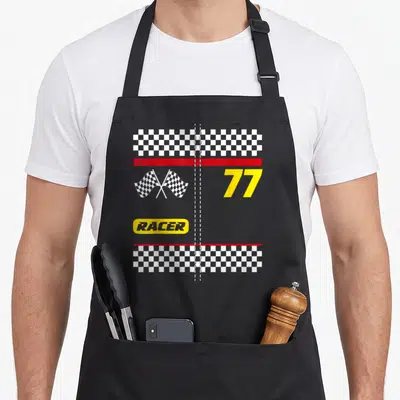 Wowsome funny halloween apron - Racing number 77 with crossed checkered flags and RACER text in yellow oval — shown on a black cotton canvas apron against a white background