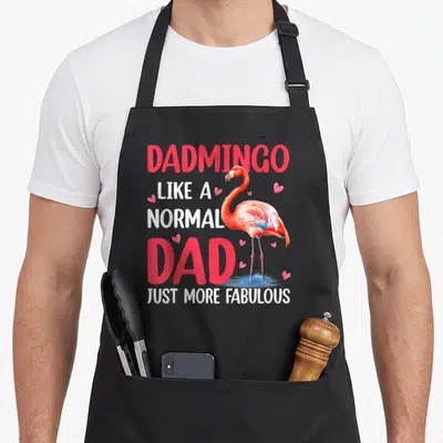 Dadmingo father day apron - Cartoon flamingo in pink and blue overlapping stacked text reading DADMINGO LIKE A NORMAL — shown on a black cotton canvas apron against a white background