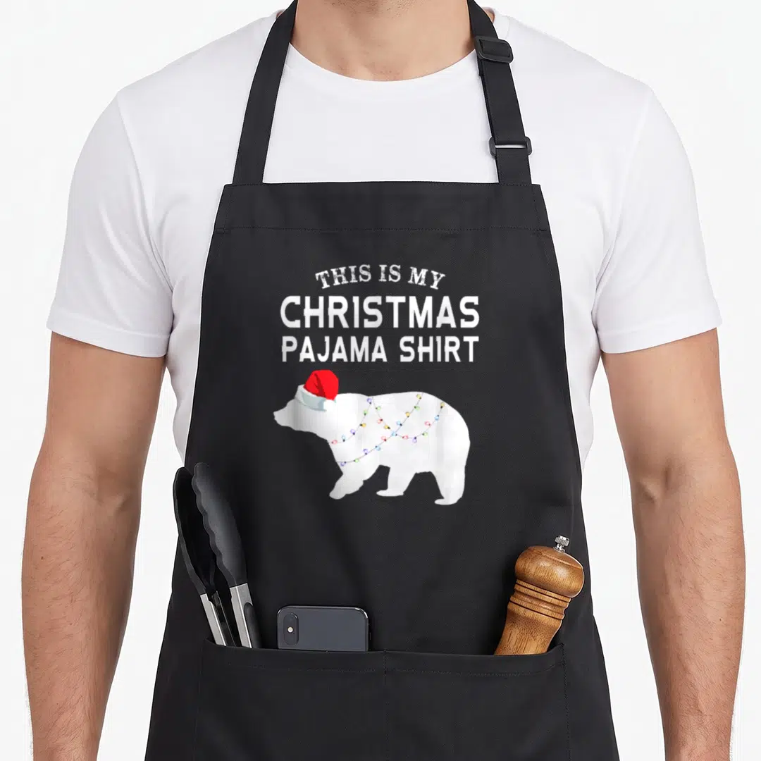 Bear family christmas aprons - Polar bear in red hat wrapped in colored lights under stacked white text — shown on a black cotton canvas apron against a white background