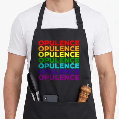 Opulence gay pride apron - Seven stacked OPULENCE words in rainbow colors red orange yellow green blue purple — shown on a black cotton canvas apron against a white background