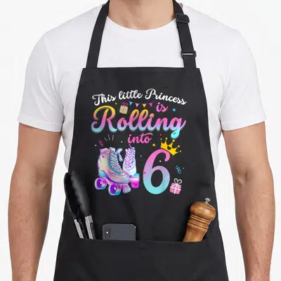 Skate 6th birthday apron - Roller skates and crowned number 6 with This little Princess is Rolling into 6 text — shown on a black cotton canvas apron against a white background