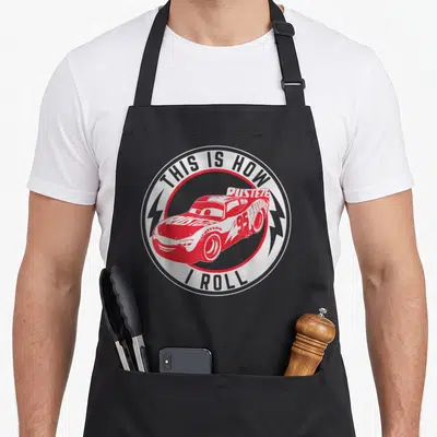 Roll car apron - Red race car with THIS IS HOW I ROLL text in circular logo — shown on a black cotton canvas apron against a white background