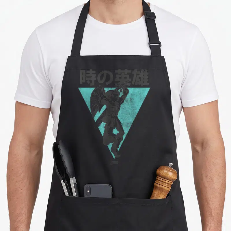 Kanji legend apron - Link holding sword and shield inside teal triangle with Japanese text — shown on a black cotton canvas apron against a white background