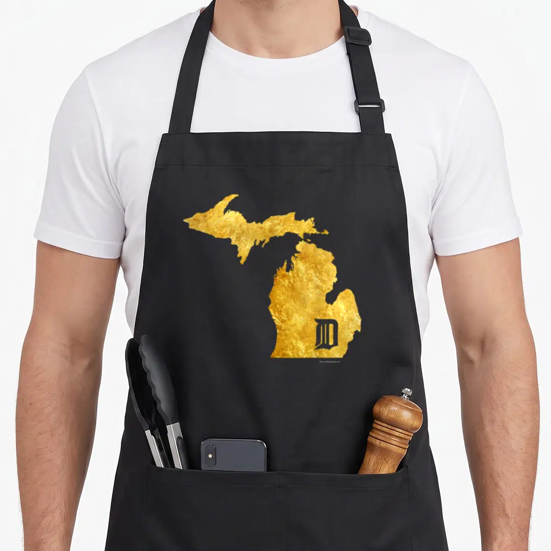 Mitten detroit apron - Gold foil Michigan state map with grey stylized D in lower peninsula — shown on a black cotton canvas apron against a white background