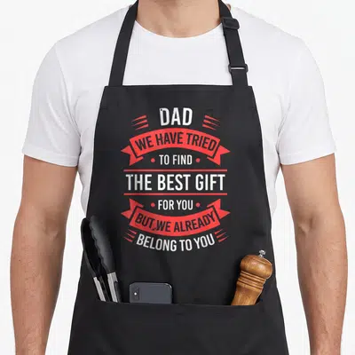 Father daddy aprons - Vertical white text stacked between red ribbons and red dots reading DAD WE HAVE TRIED TO FIND — shown on a black cotton canvas apron against a white background