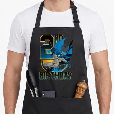 Action 2nd apron - Leaping Batman over large number 2 and yellow bat signal with 2nd Birthday text in blue and grey — shown on a black cotton canvas apron against a white background