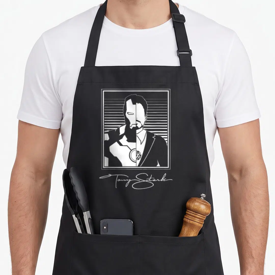 Tony split apron - White split portrait of Tony Stark face and helmet in rectangle with signature below — shown on a black cotton canvas apron against a white background